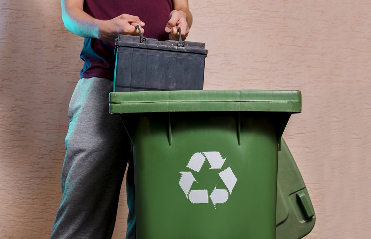 Man throwing old car battery in recycle bin.