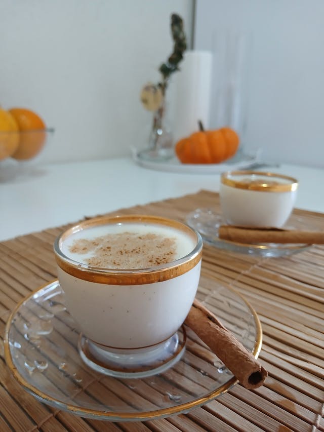 Cup of coffee with pumpkin spice creamer surrounded by autumn decor