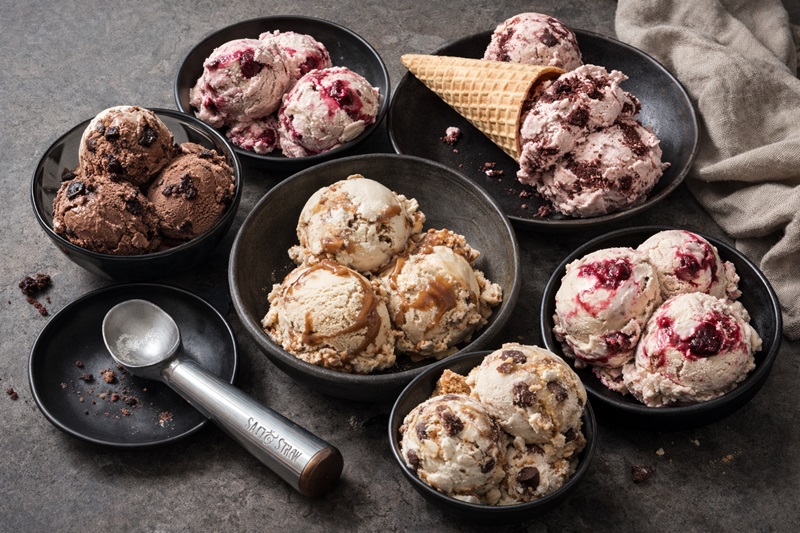 Dairy-free ice cream scoops in ceramic bowls, featuring fruit-based sorbets and plant-based flavors on a dark stone surface.