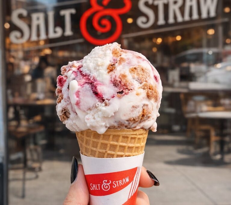 Hand holding a waffle cone with a scoop of ice cream outside a Salt & Straw shop