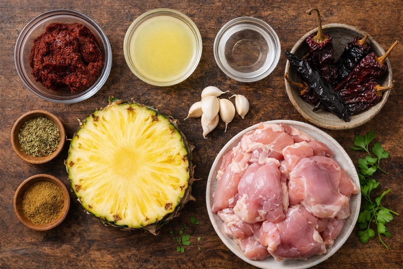 Ingredients for chicken al pastor marinade including achiote paste, guajillo chiles, pineapple, and chicken thighs