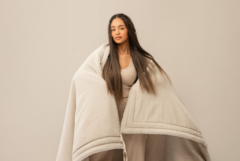 Woman standing wrapped in an oversized cream-colored quilt